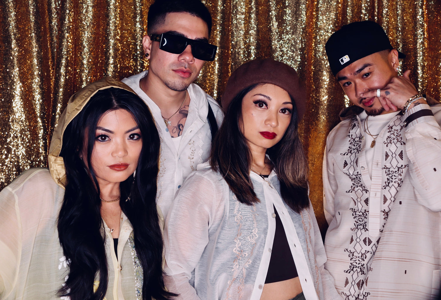 Two Filipina women and 2 Filipino men are posing in front of a sequin curtain wearing different styles of barong hoodies.