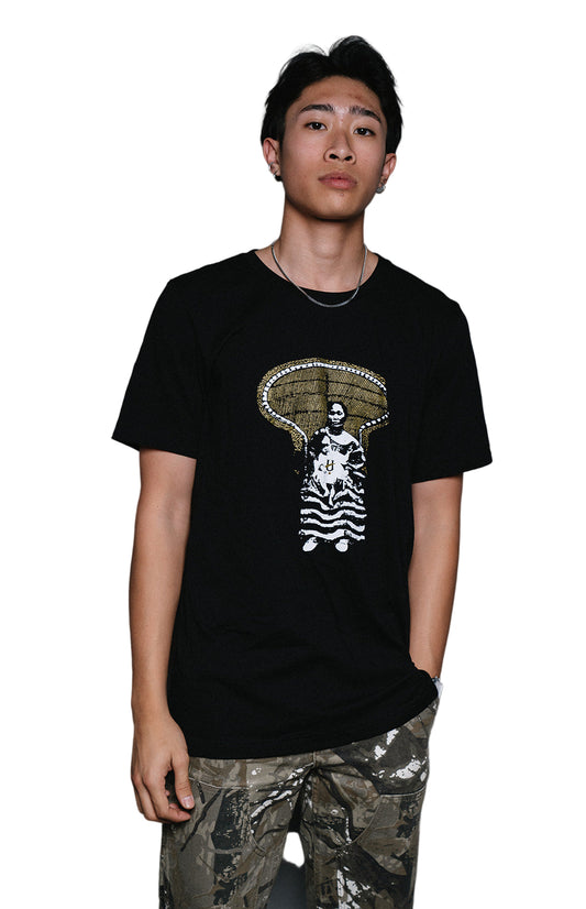 A person wearing a black t-shirt with a graphic print of a peacock throne on the front, paired with camouflage pants.