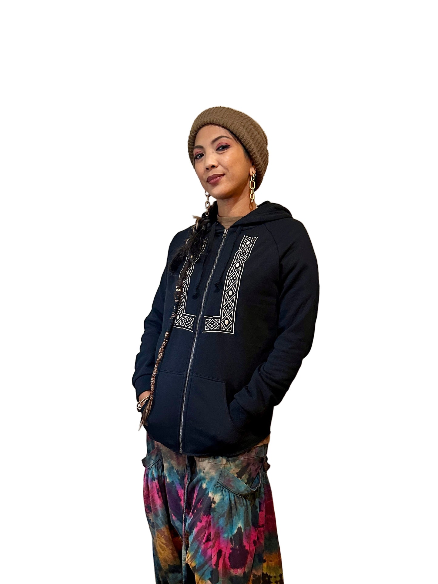 Person wearing a black barong zip up hoodie with embroidery and colorful baggy pants and beige beanie.