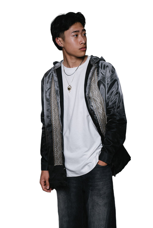 A person wearing a long sleeve, button down gray ombré with ivory embroidery and a silver hoodie.