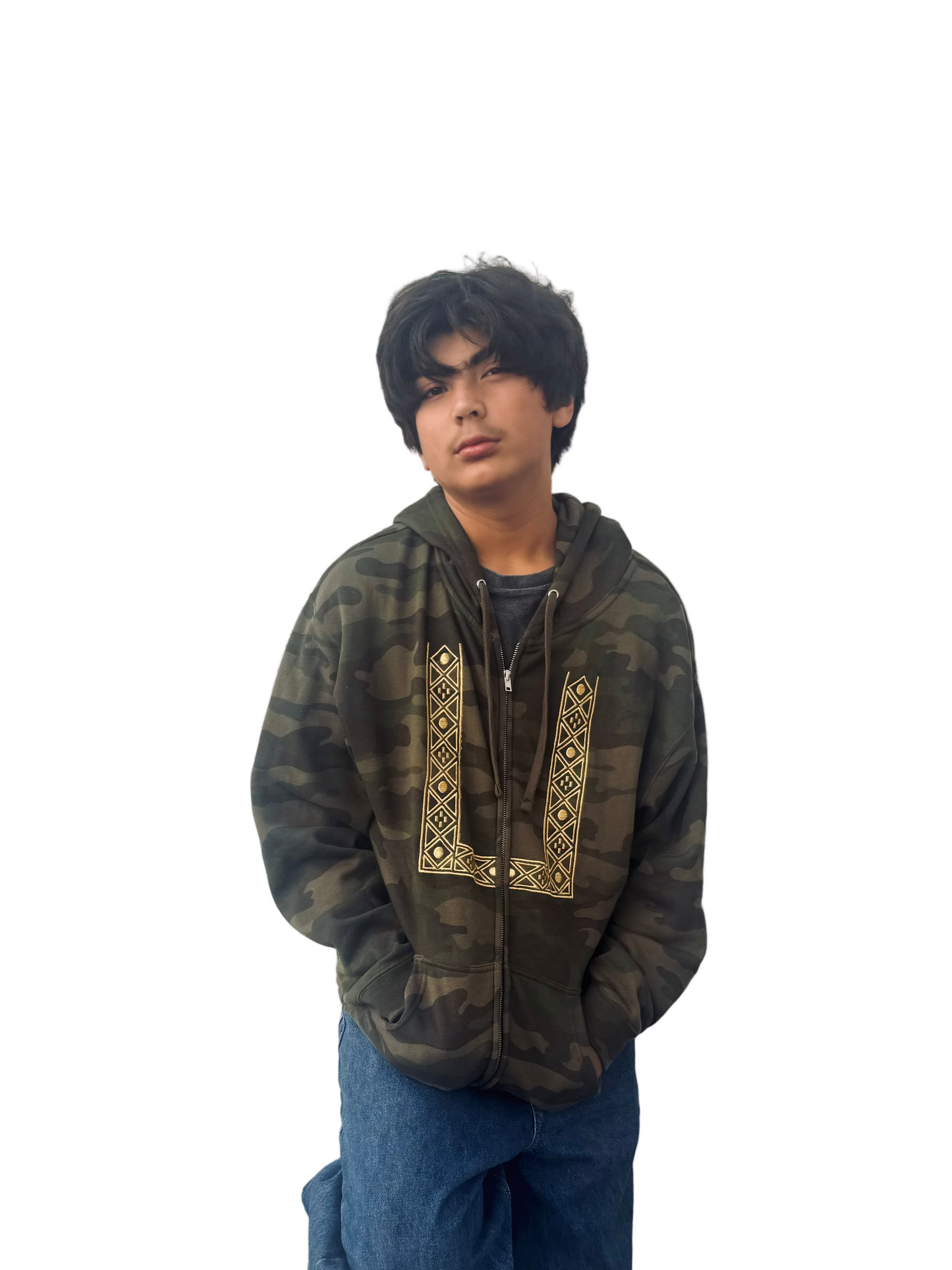Person wearing a camouflage zip up hoodie with gold geometric barong embroidery and blue jeans against a white wall.