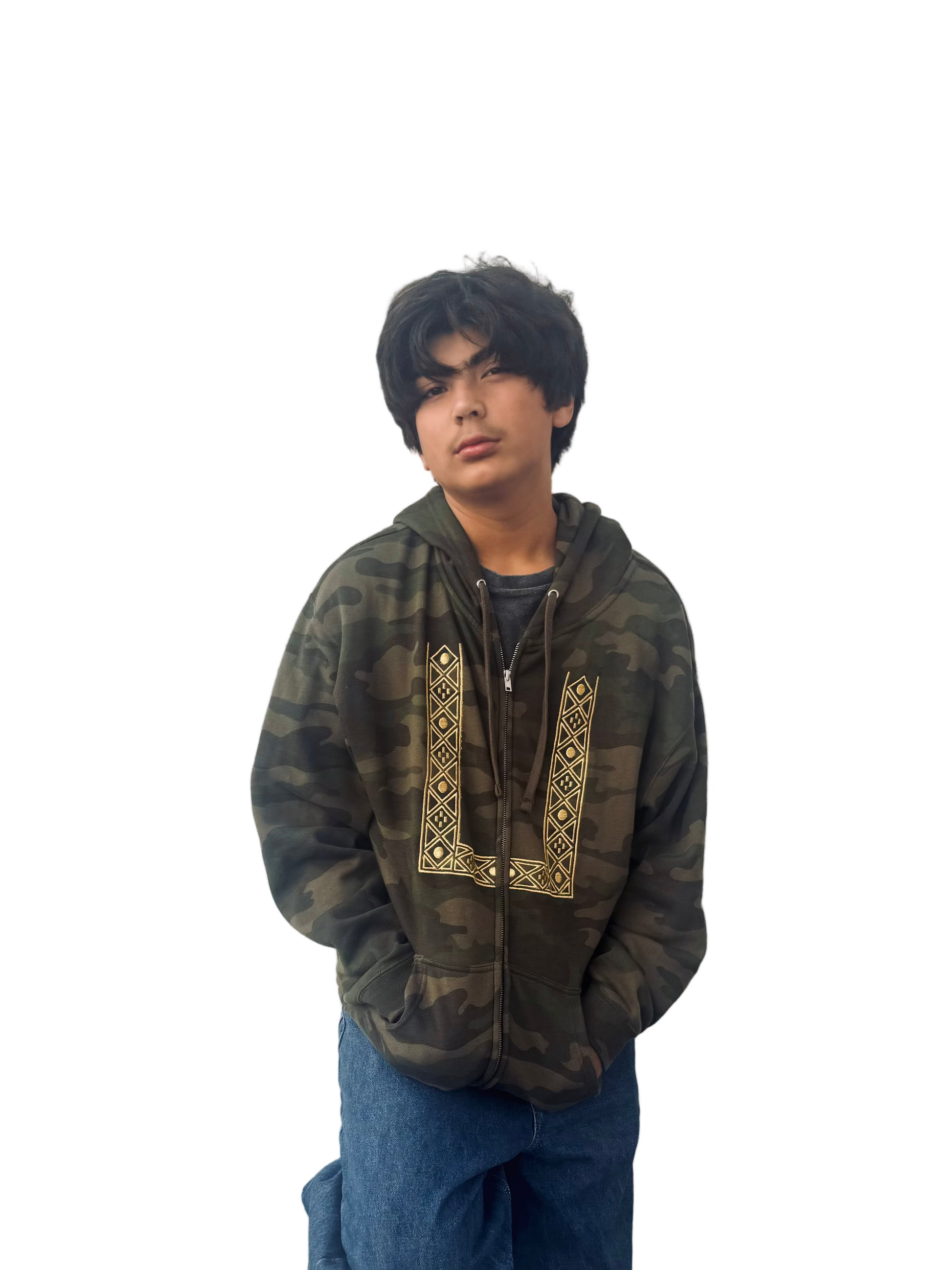 Person wearing a camouflage zip up hoodie with gold geometric barong embroidery and blue jeans against a white wall.