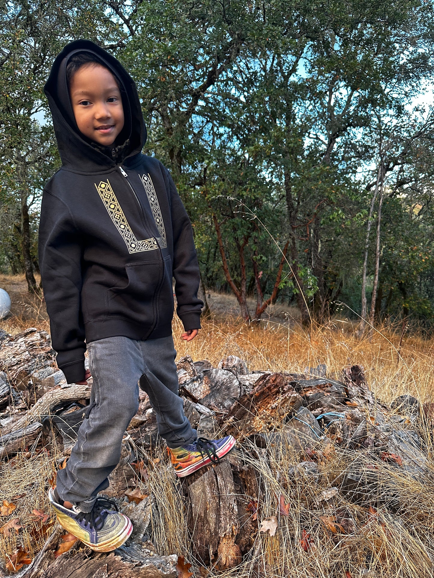 Child wearing his barong hoodie, standing on a log in a forest setting