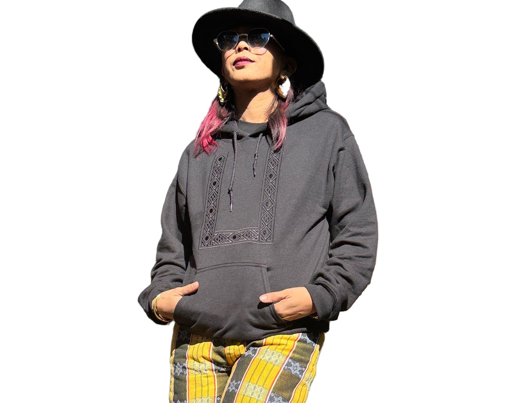 Person wearing a gray hoodie with intricate designs, black hat, and yellow plaid pants on a white background